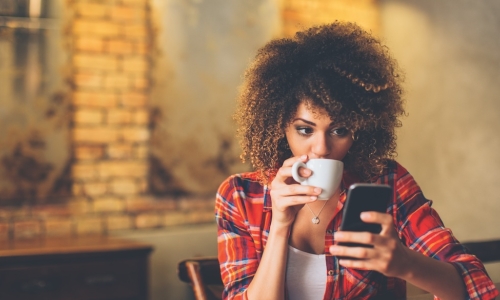 Gen Z woman drinking coffee and using smartphone for online banking at a cafe