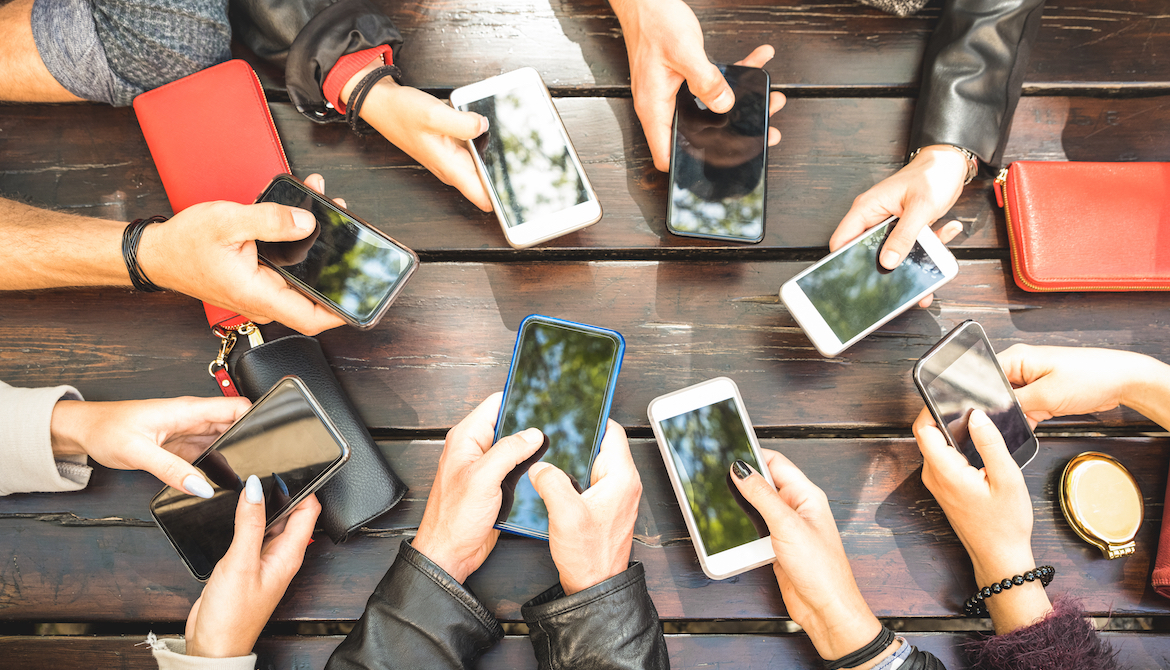 group of millennials' arms with phones around table