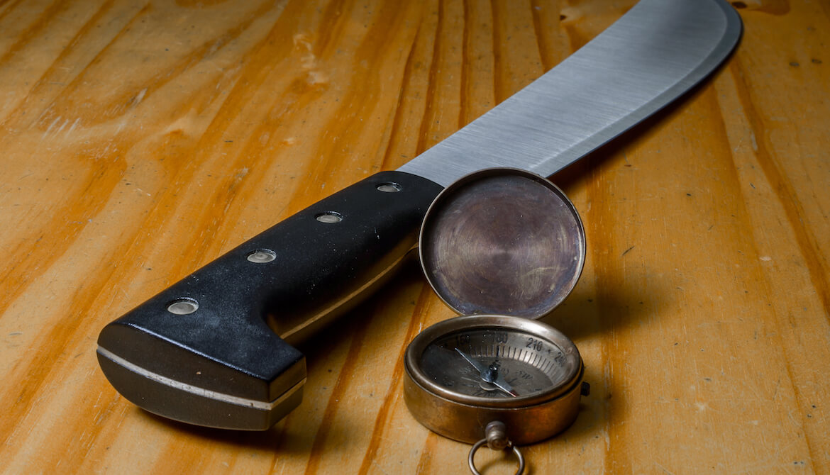 Machete and compass in wood background
