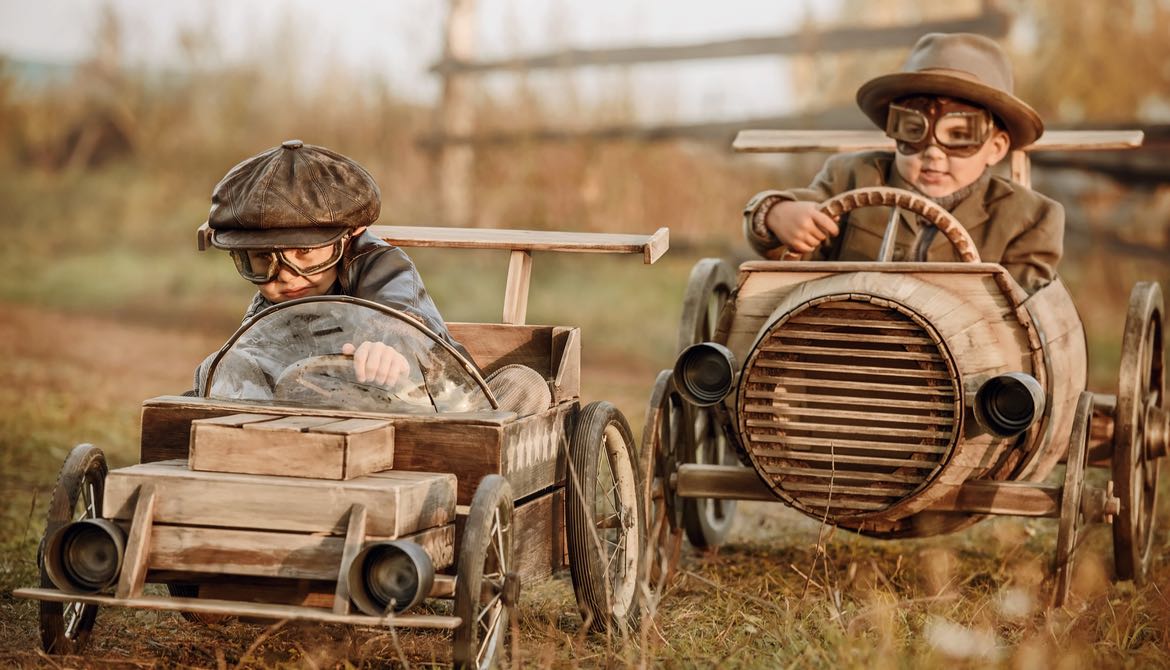 Two boys in helmets and goggles racing in wooden toy cars
