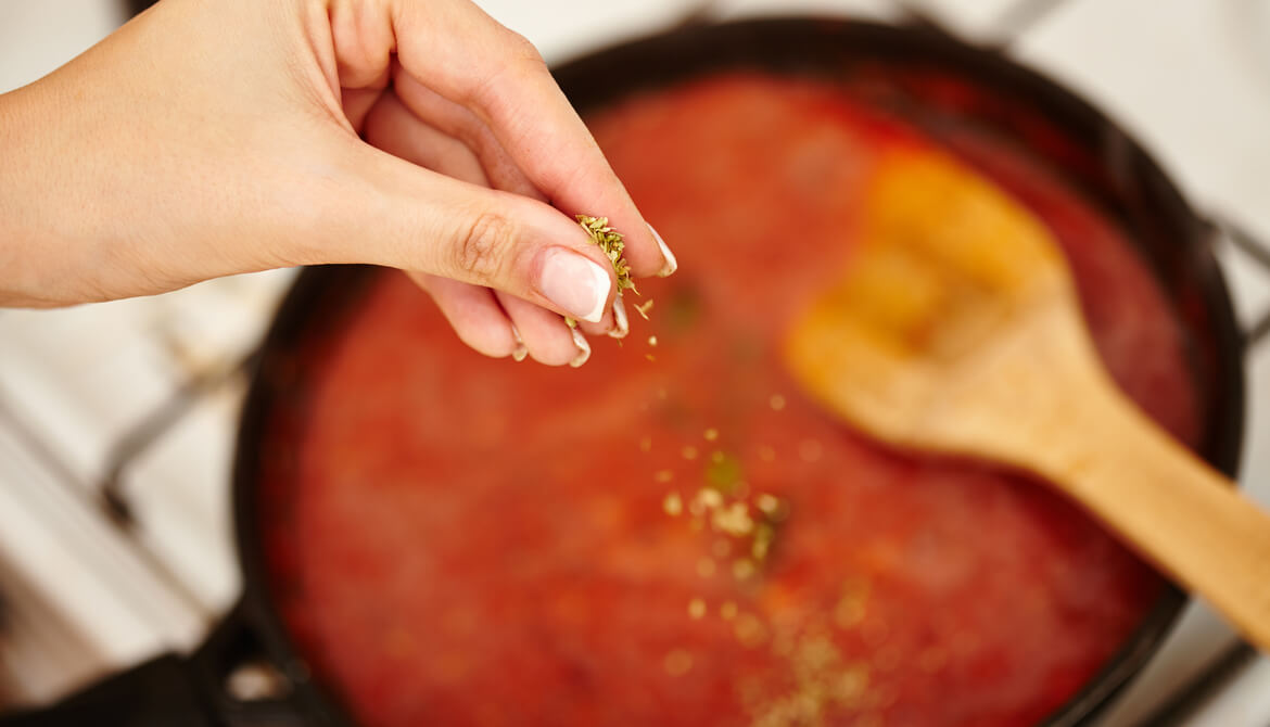 Hand adding ingredients to a tomato sauce