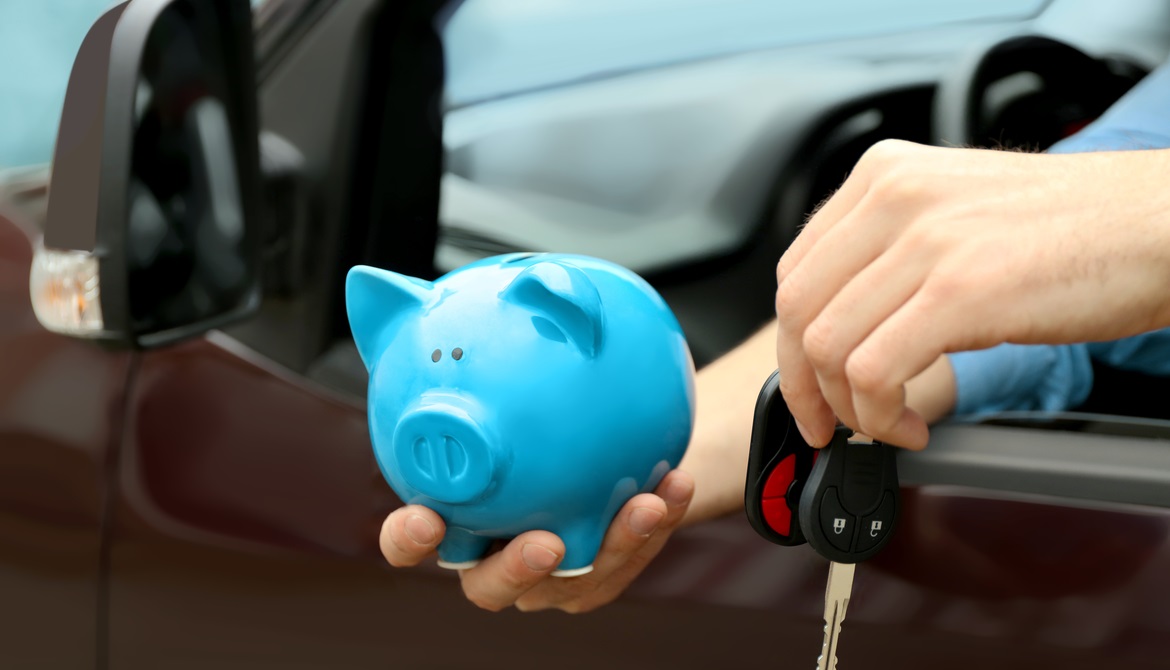 man holding blue piggy bank and car keys out car window