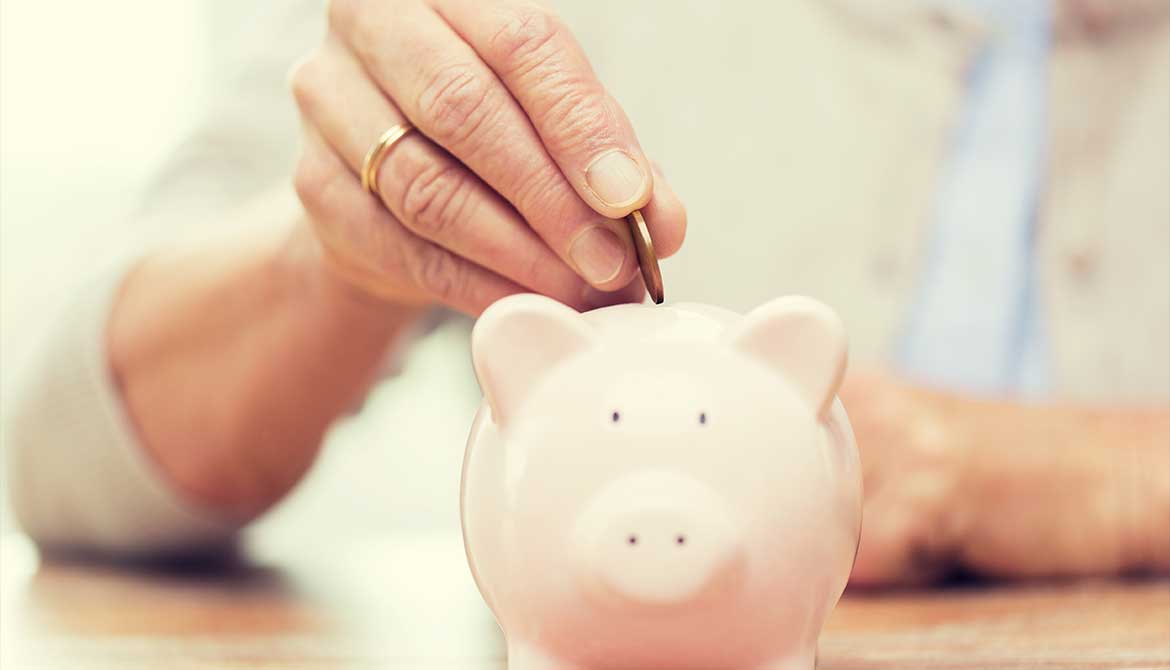 older woman’s hand putting a coin into a piggy bank