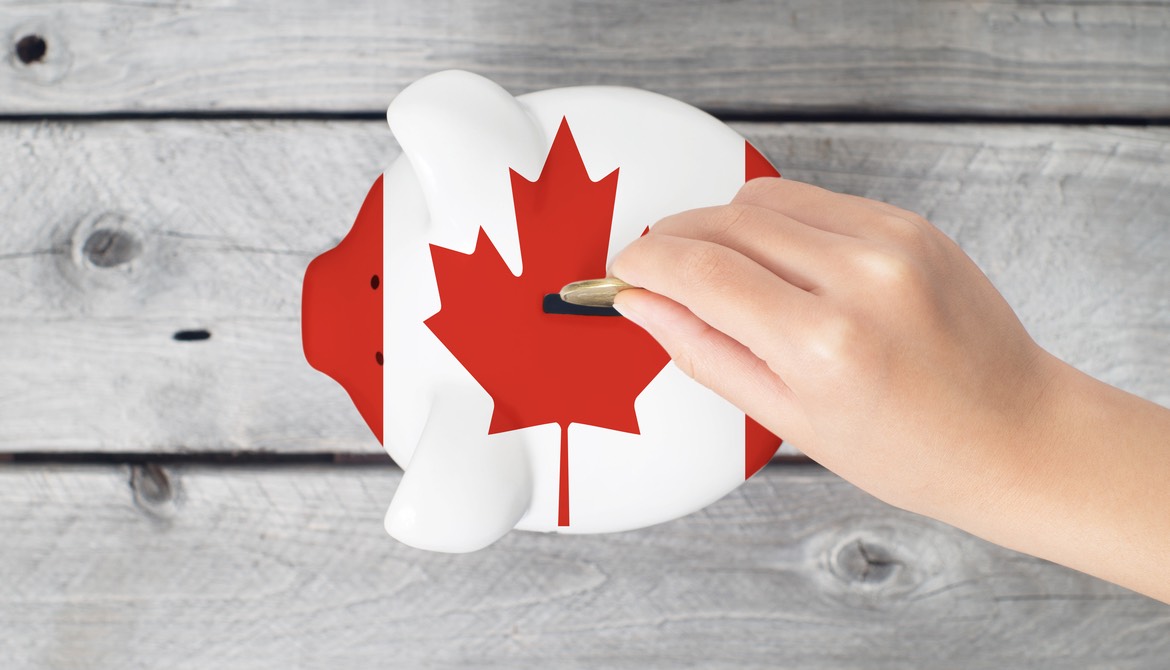 hand dropping coin into piggy bank painted to look like Canadian flag