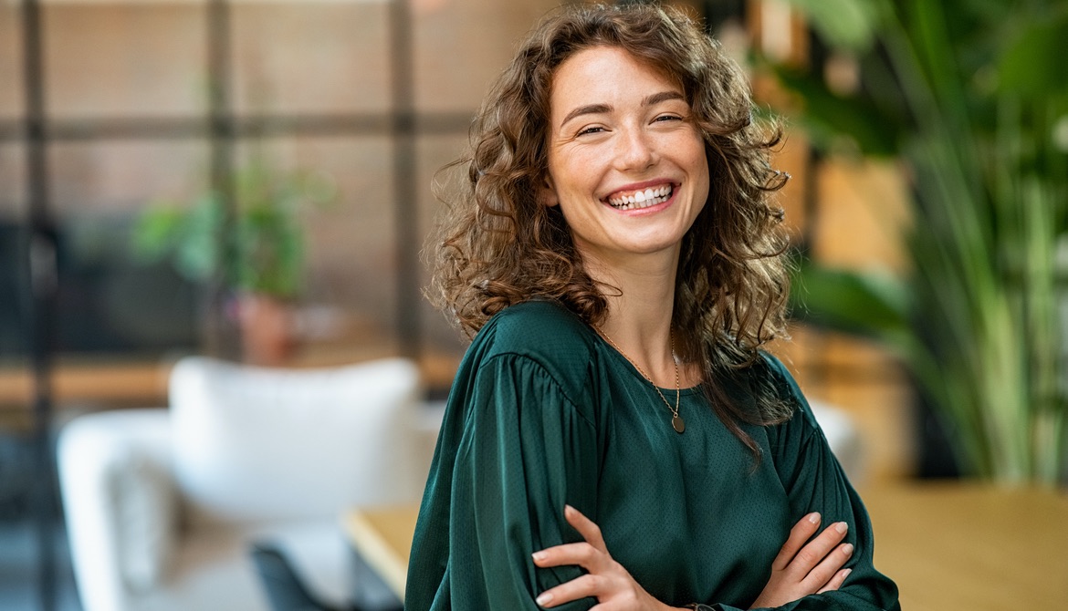 woman in green shirt with light brown curly hair smiling confidently at camera