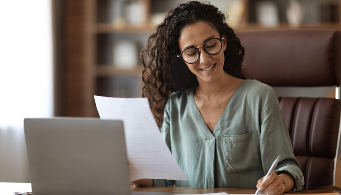 woman smiling writing while holding paper in other hand