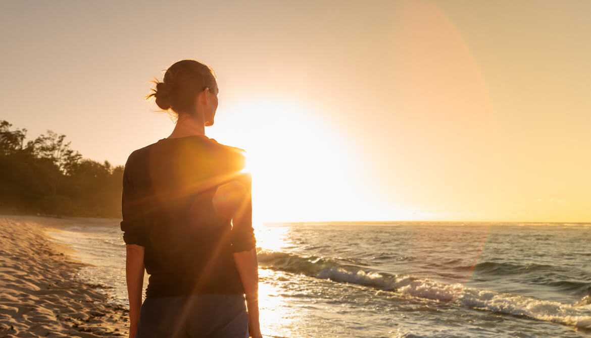 woman in silhouette looking out over the waves on the beach