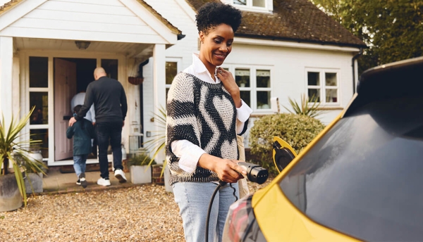 woman charges electric vehicle while husband and son enter the front door of new home