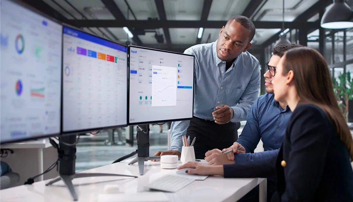 individuals looking at a 3 monitor set up while talking