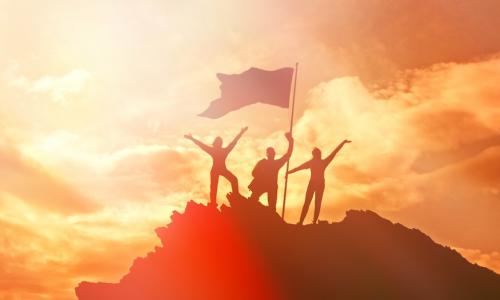 Group of people raising a flag at the top of a mountain symbolizing high performance and success