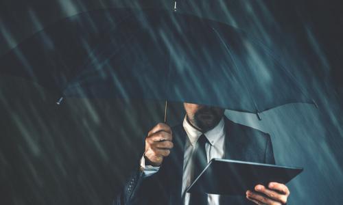 business man holds tablet under an umbrella on a dark rainy day