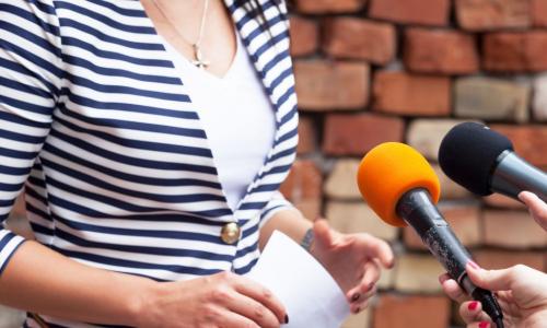 businesswoman in striped jacket speaking to interviewers with microphones
