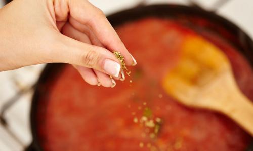 Hand adding ingredients to a tomato sauce