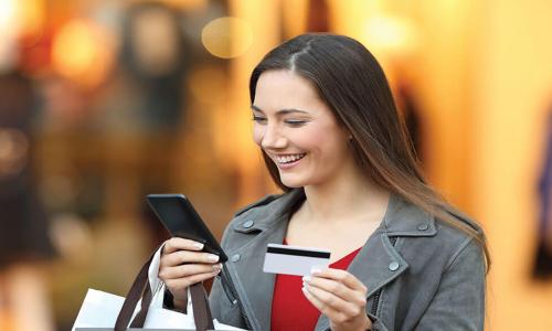 happy woman holding credit card and shopping bags while looking at smartphone