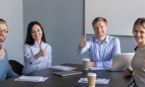 young executives around a table giving thumbs up