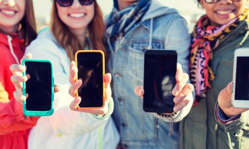 close up of happy teenage friends showing blank smartphone screens outdoors