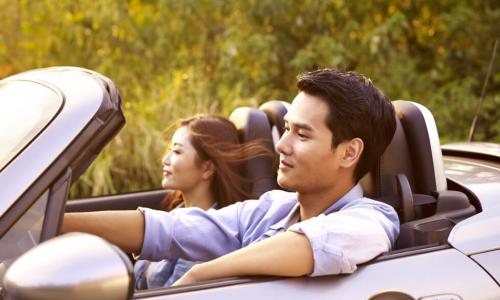 young asian couple riding in a convertible sport car at sunset