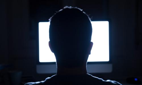 Man sitting in dark in front of bright white computer screen