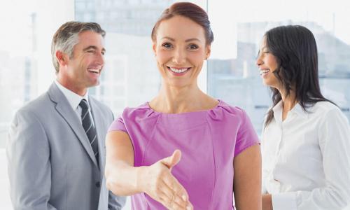 female CEO in purple dress reaching out hand toward viewer to shake