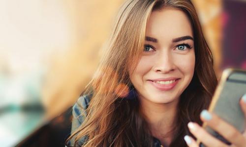 smiling young woman using smartphone in café