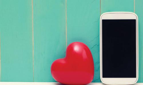 white smartphone next to shiny red heart in front of green wooden wall