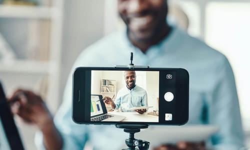 smartphone camera on tripod filming smiling Black businessman presenting a chart to viewers