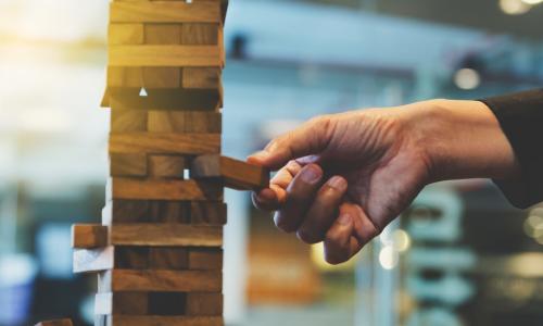 businessperson’s hand reaching out to place or pull a wooden block from a Jenga game tower