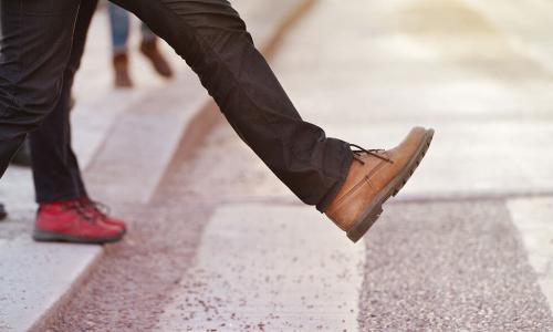 person wearing brown leather shoes about to take a big step from curb into crosswalk
