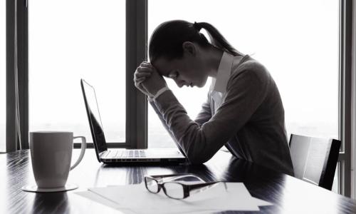 depressed female employee sitting alone at desk with head bowed