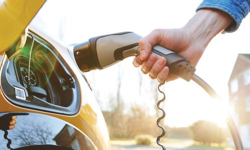 hand reaches out to plug in electric vehicle charger