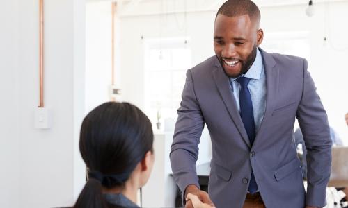 HR manager greeting and shaking hands with seated female job candidate at interview