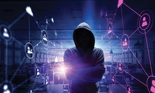 hacker in hoodie standing in darkened office full of computers with an image of a network of connected people floating in the background