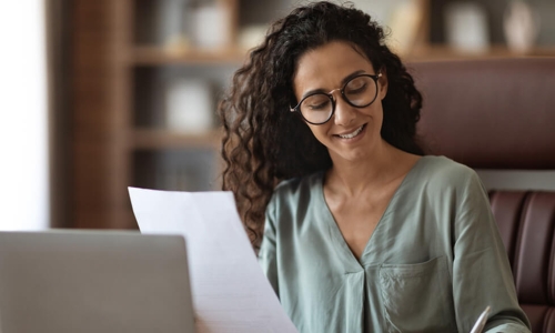 woman smiling writing while holding paper in other hand
