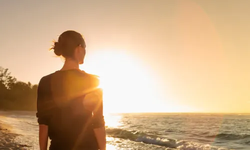 woman in silhouette looking out over the waves on the beach