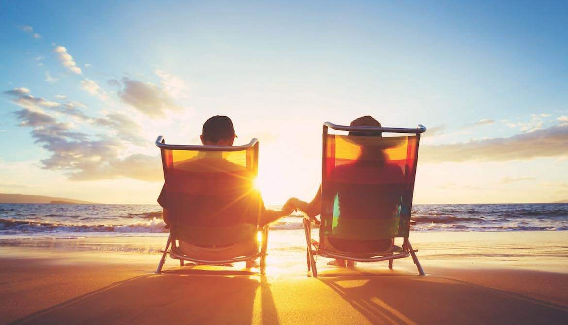 Retired couple sitting on chairs at the beach at sunset
