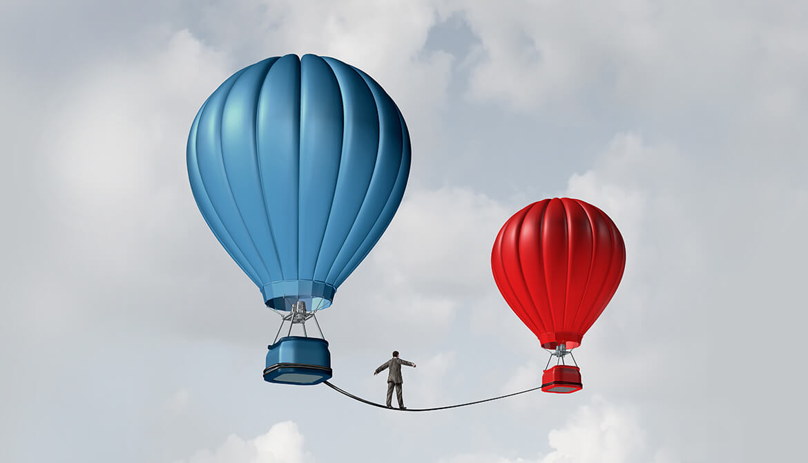 A business man walks a tight rope from a blue hot air balloon to a red one