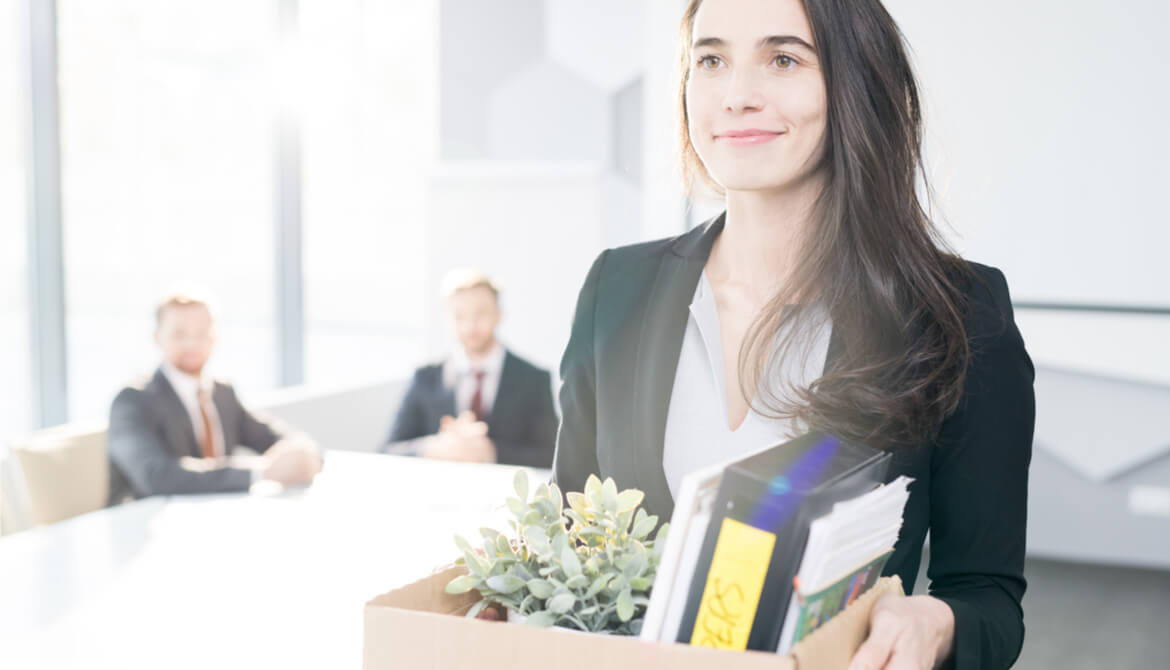 smiling young businesswoman holding box of personal belongings leaving office after quitting job