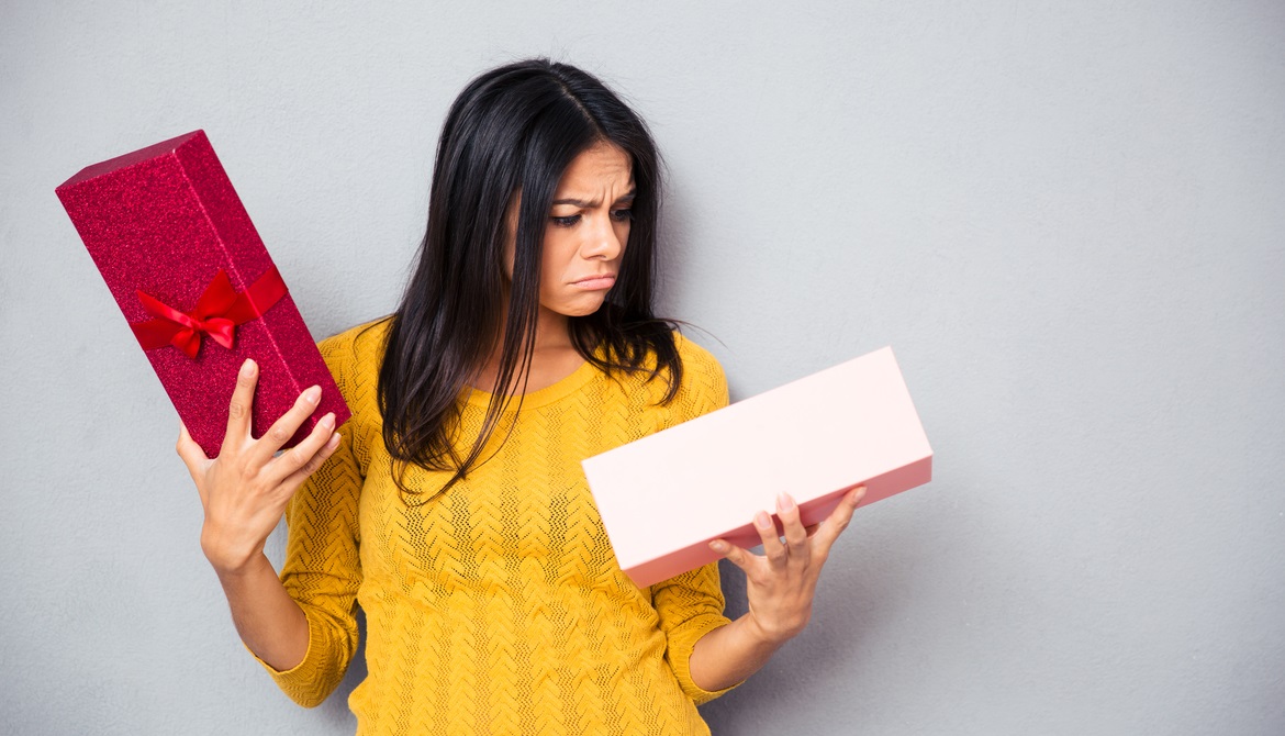 young woman in yellow sweater looking sadly into an open holiday gift box