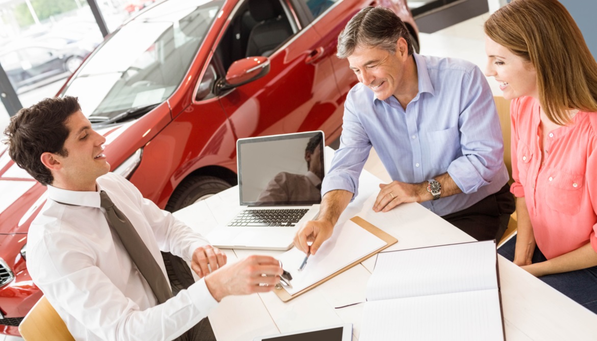 customers and car salesman at dealership desk signing papers