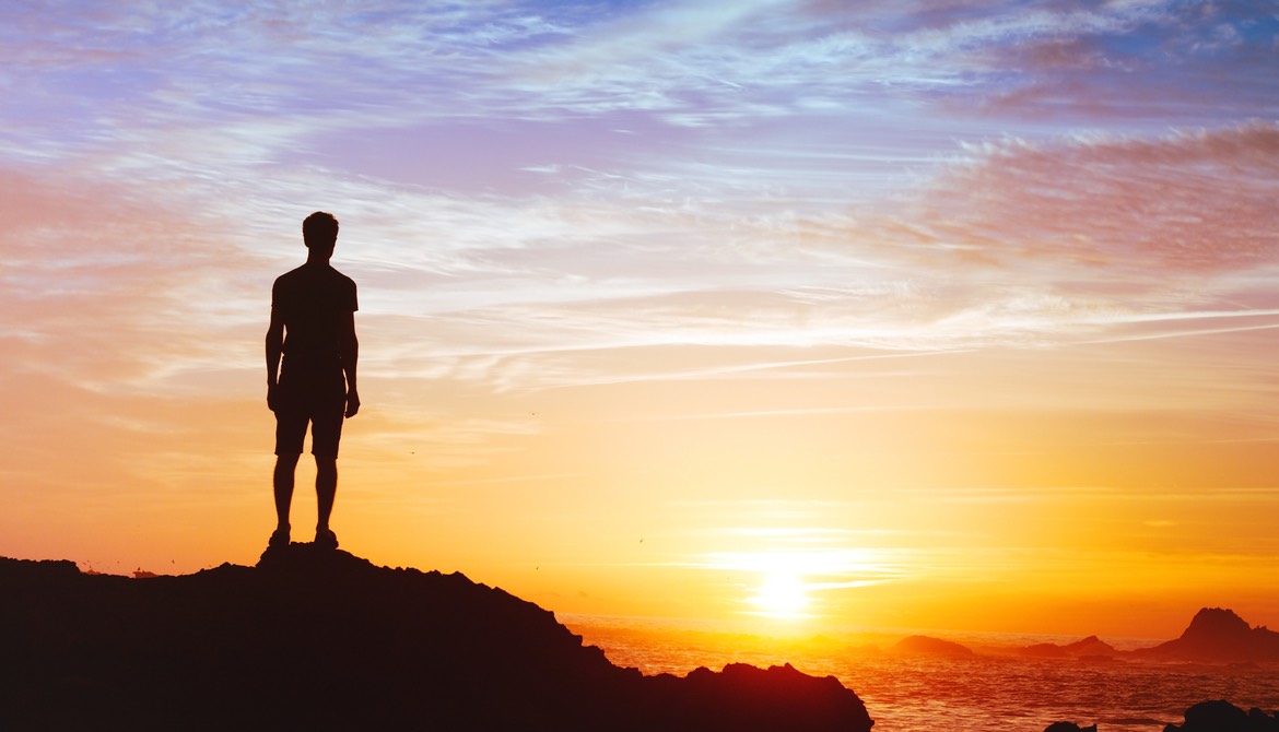 man standing on hill with sunset