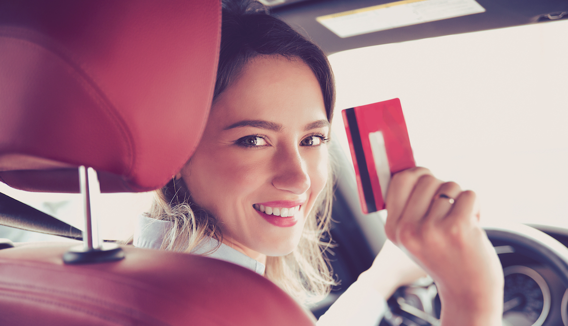 Happy woman sitting inside a new car and holding up her credit card