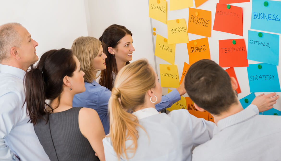 Business colleagues brainstorming multicolored labels stuck on whiteboard in meeting