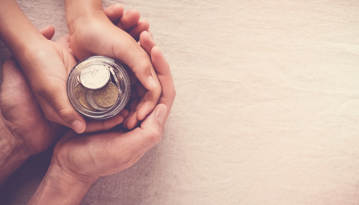 adult hands holding child's hands around a savings jar