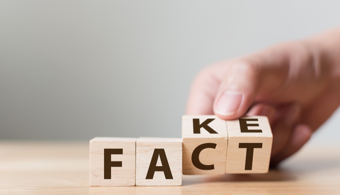 hand flips wooden blocks to change the word fake to spell fact