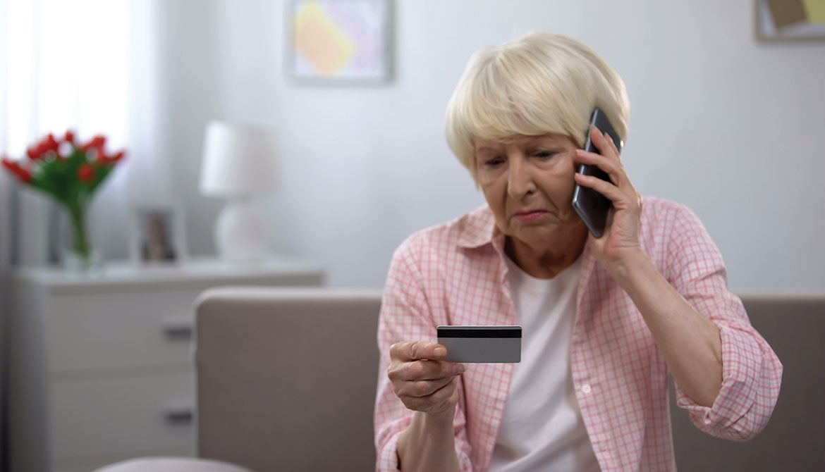 upset elderly woman on phone looking at credit card