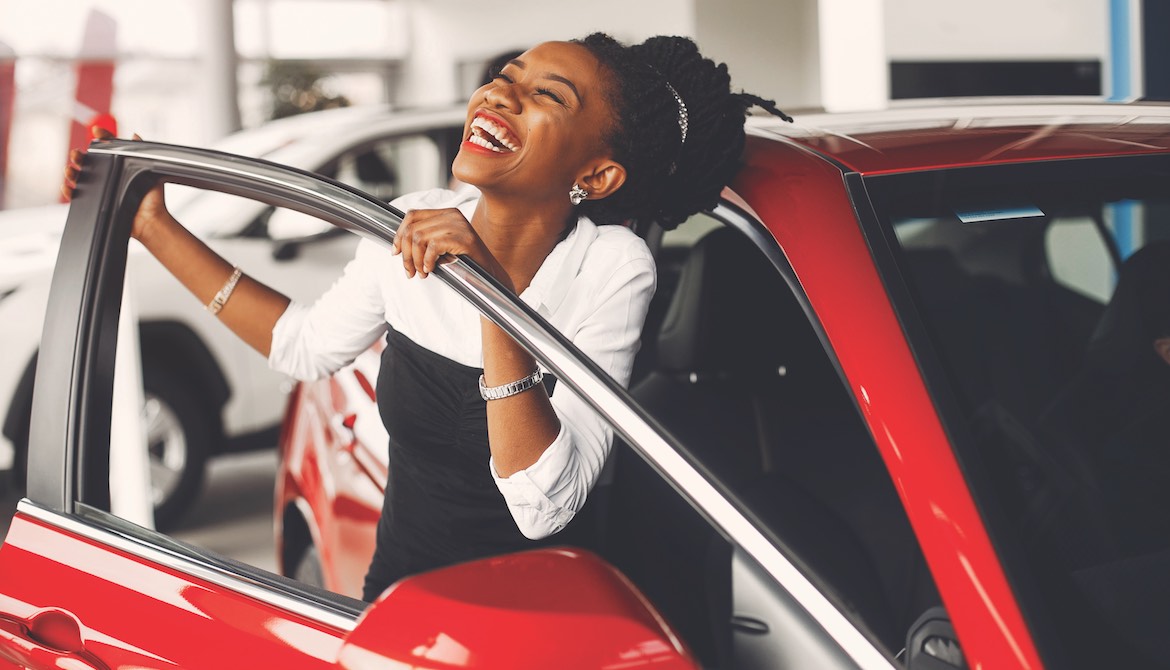 excited young African American woman smiles next to new red car
