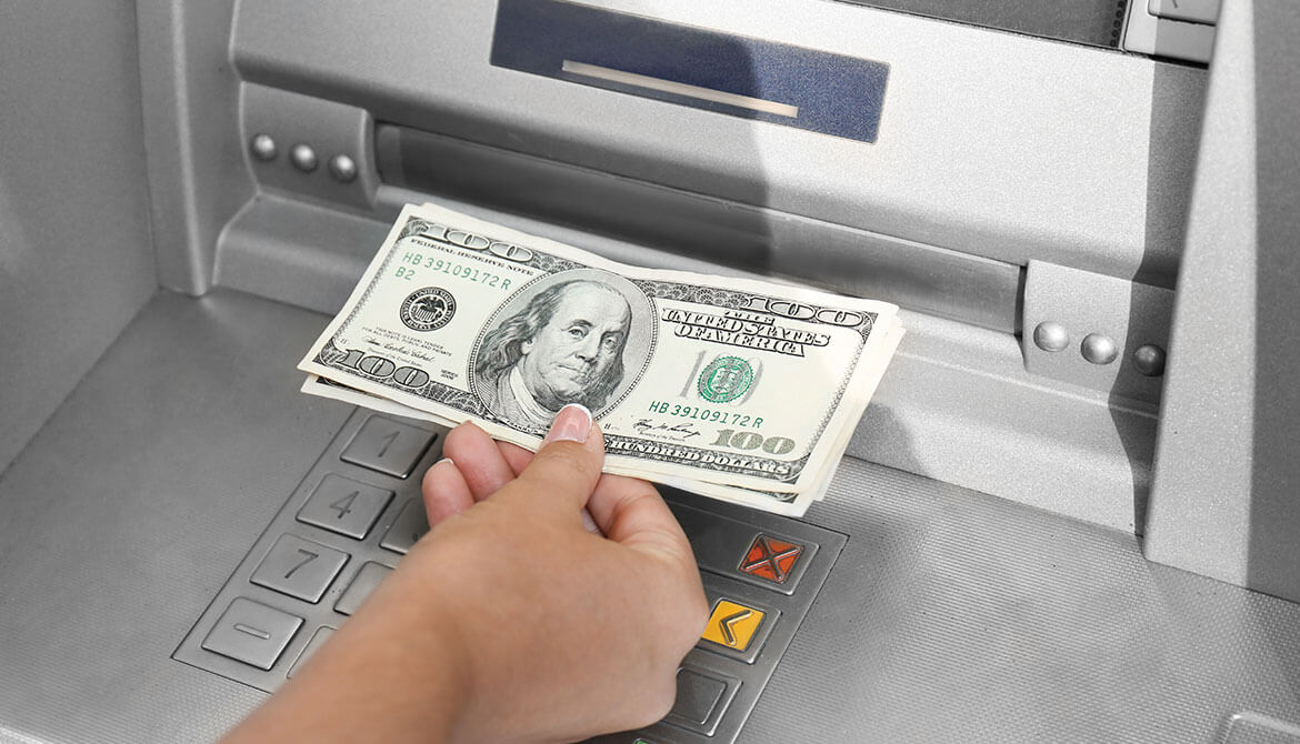 hand withdrawing $100 bills from ATM