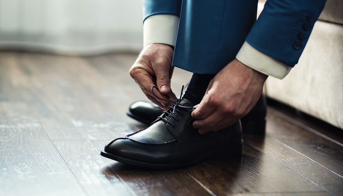 businessman in blue suit bending down to tie laces of black dress shoe