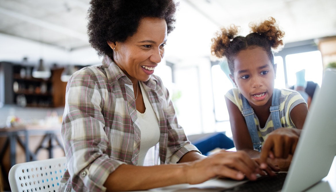 African American mother and daughter work on laptop together at home
