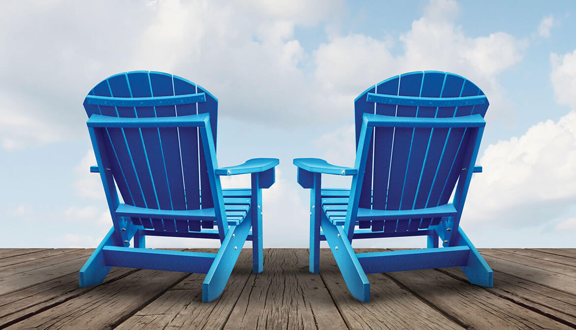 pair of blue Adirondack chairs on wooden deck facing blue sky